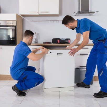 Two Young Male Movers In Uniform Placing Dishwasher In Kitchen